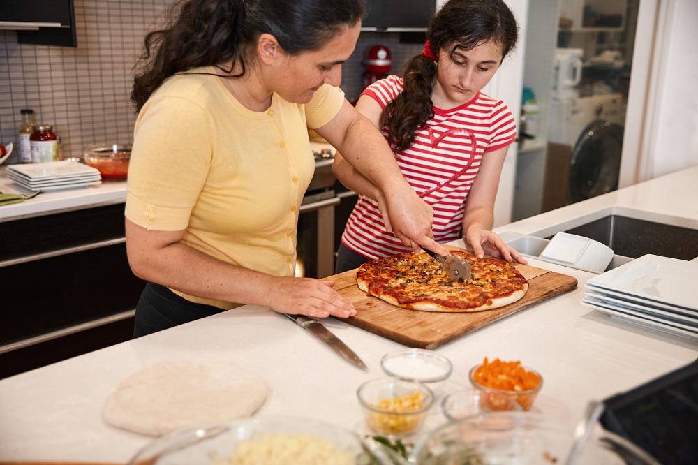 Mum and older girl cooking pizza together in the kitchen.