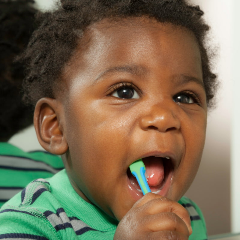Image of a smiling toddler brushing their teeth.