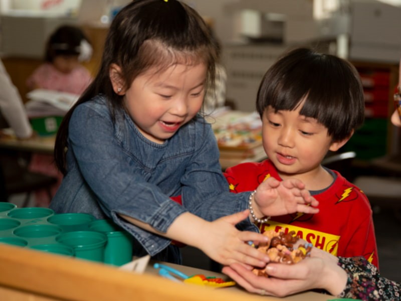 Image of two young children sitting at a table and playing with toys together.