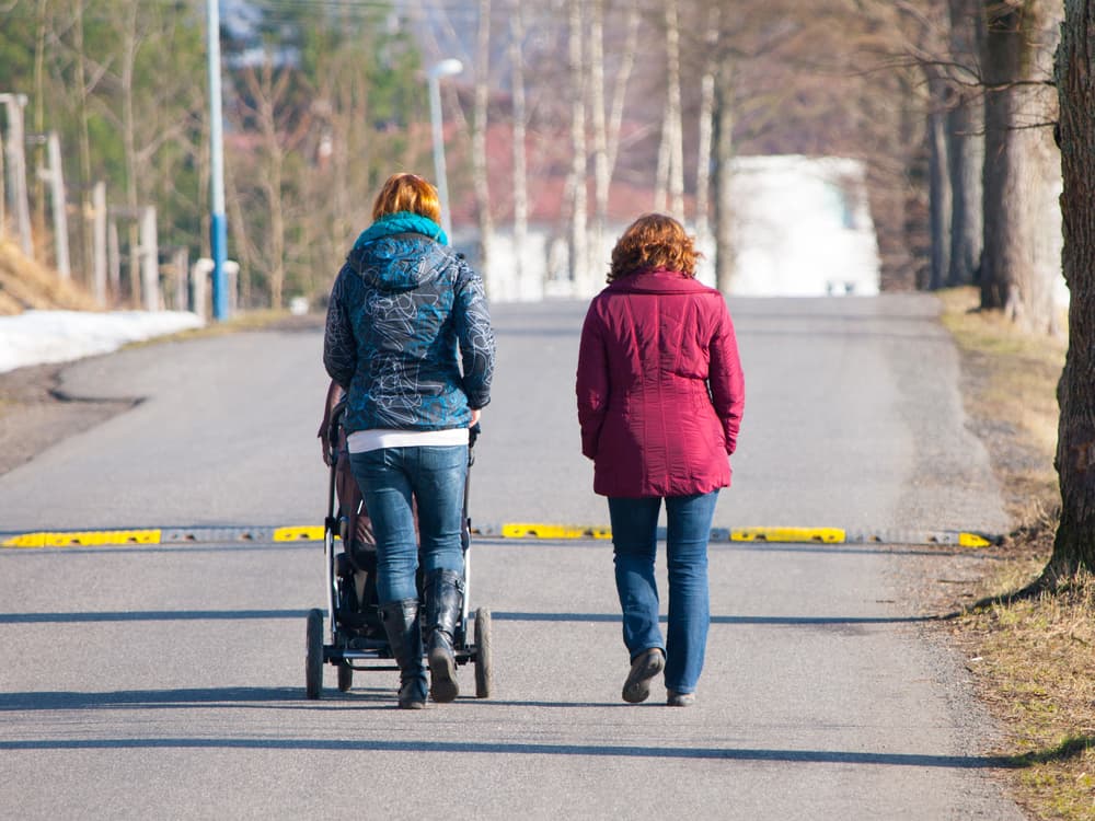 Image of two adults walking away from the camera, with one adult pushing a pram.