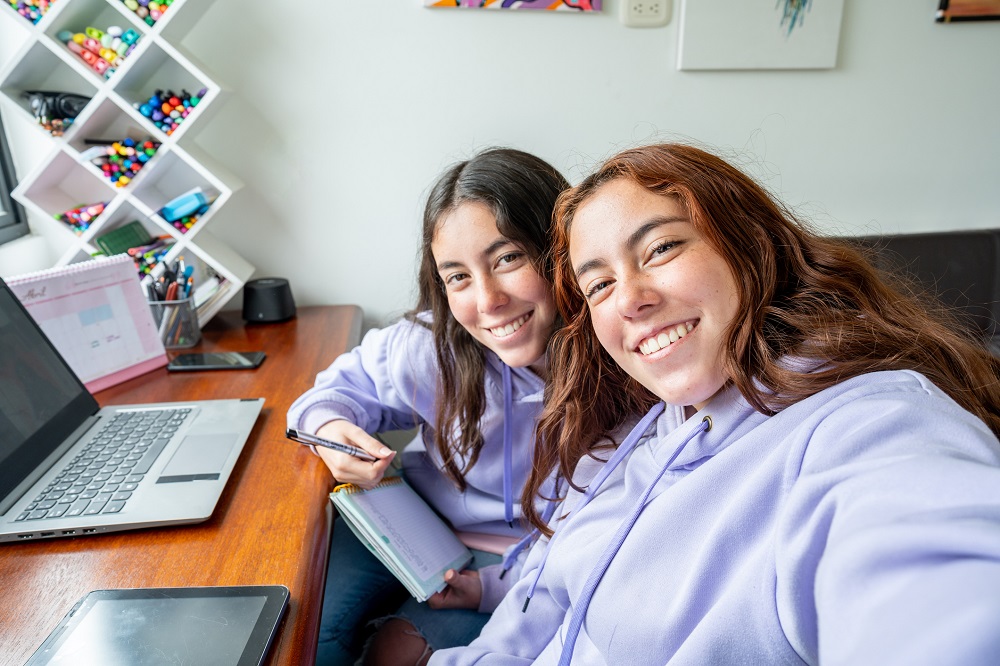 Twin teen girls smiling, with an open laptop next to them