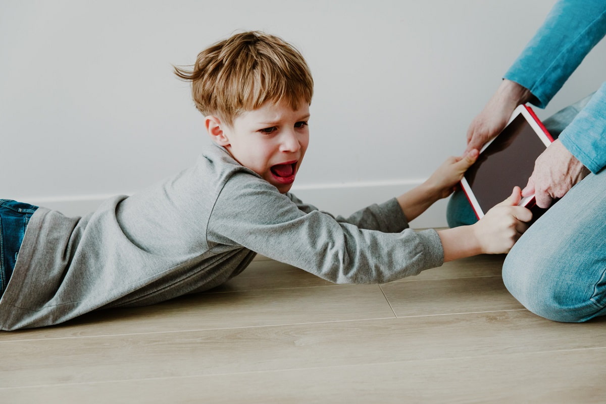 Young boy screaming and hanging onto a tablet his mother is trying to take away