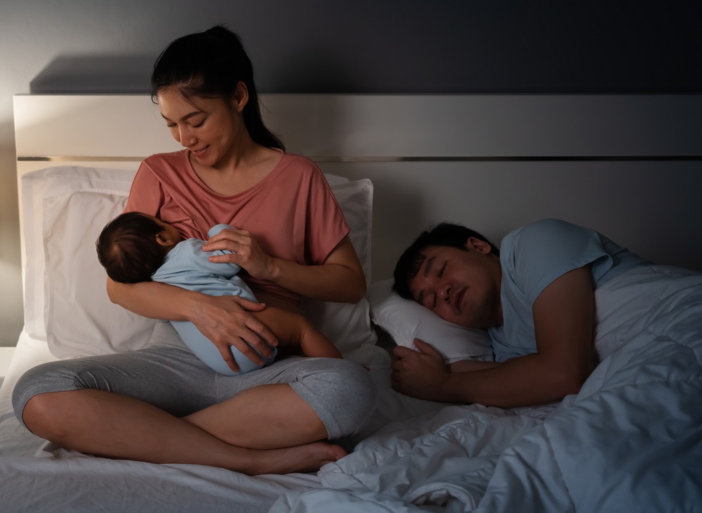 Mother breastfeeding at night with dad sleeping beside her
