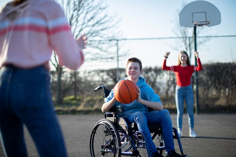 Teens playing basketball outside, one is in a wheelchair
