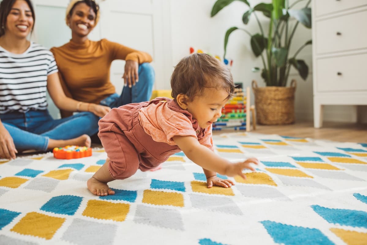 Baby crawling across a play mat watched by their mums