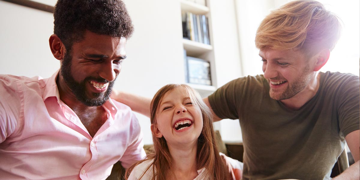 Girl sitting between her dads, laughing together