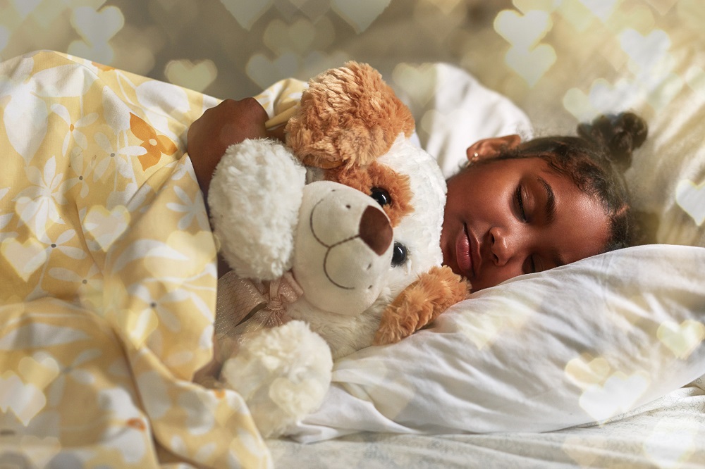 Young child asleep in bed, cuddling a large soft toy dog