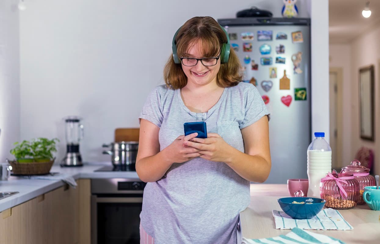 Teen girl in the kitchen wearing headphones, looking at her phone