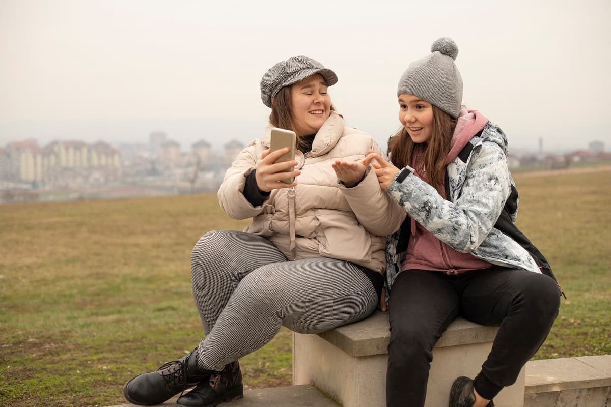Teen girls sitting outside looking at a mobile phone and laughing