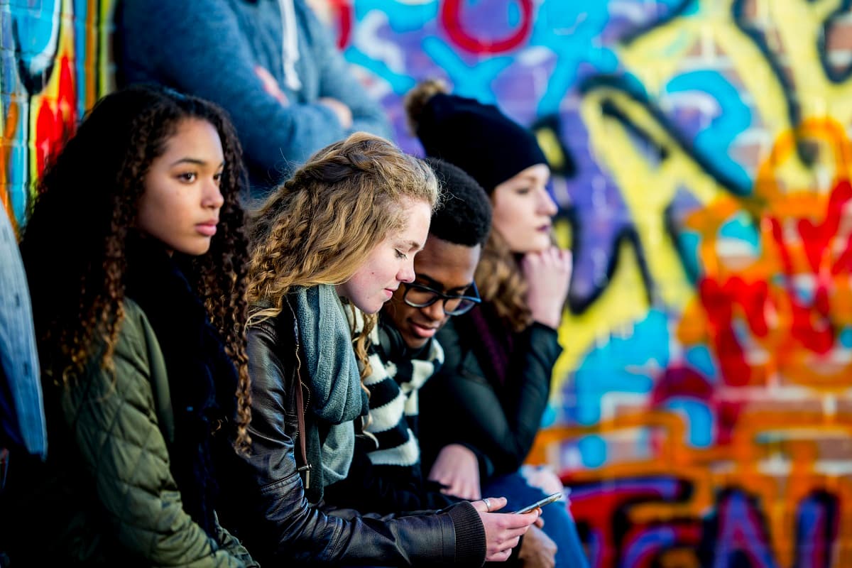 Teens sitting outside beside a wall covered in grafitti