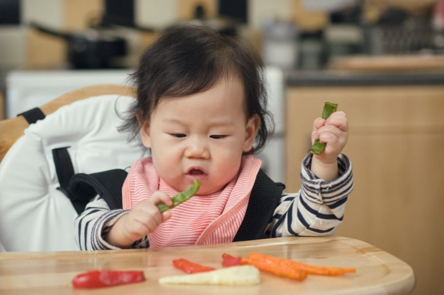 Toddler in a high chair eating vegetables