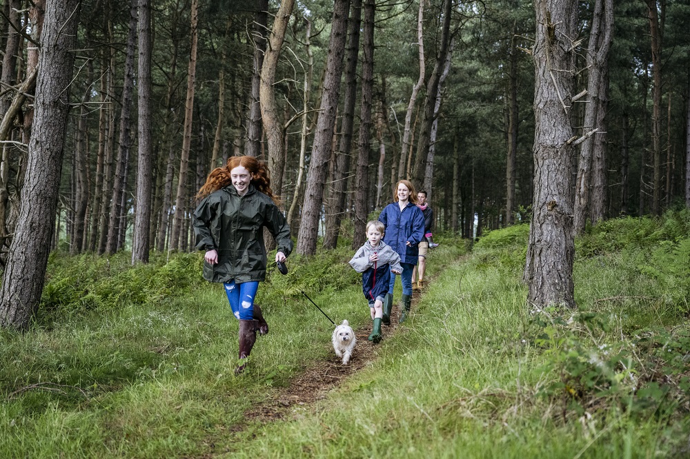 Family running through woodland with their dog