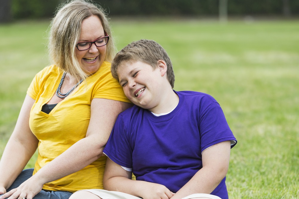 Mum and older boy sitting outside in a park laughing together