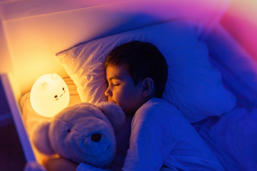 Toddler boy asleep hugging a teddy bear with a night light next to him