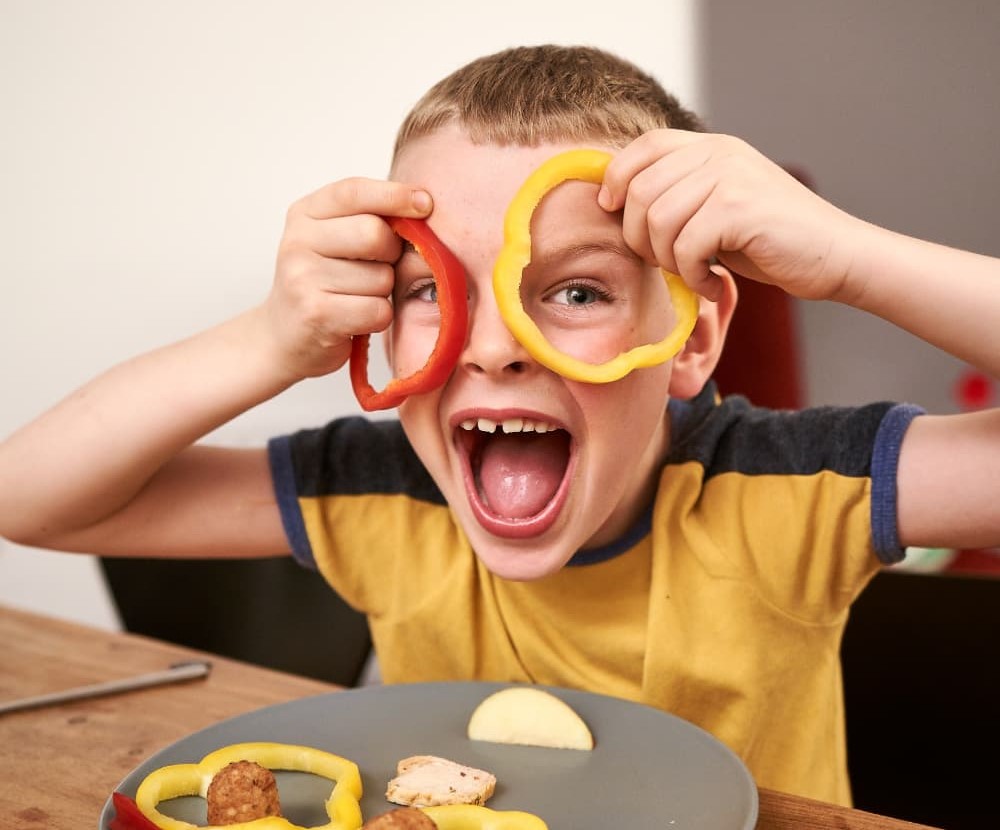 Happy boy holding rings of pepper up to his face like spectacles.