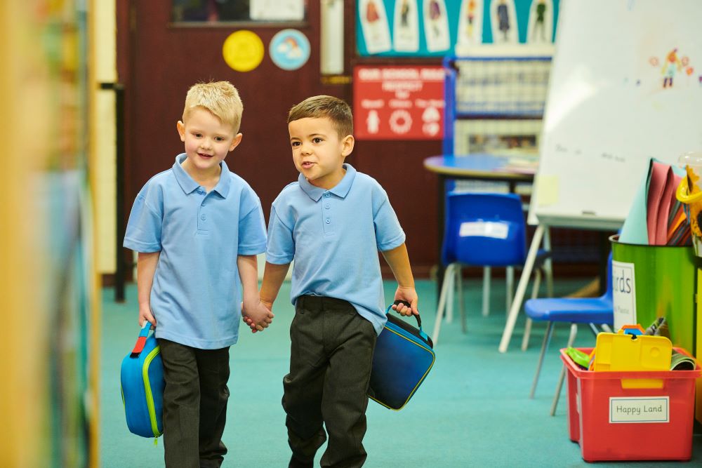 Two young boys holding hands in a classroom.