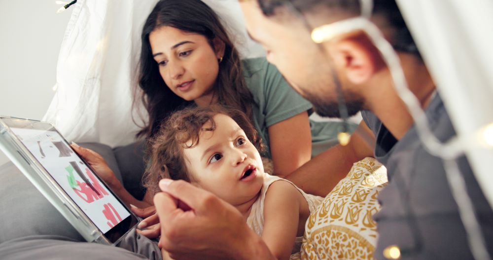 Mum and dad looking at a tablet with their toddler.