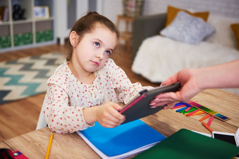 Mum taking tablet away from young girl.