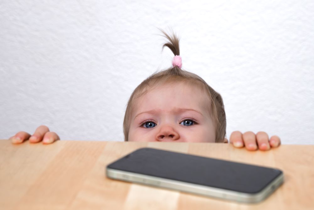 Baby looking up at a mobile phone on a table.