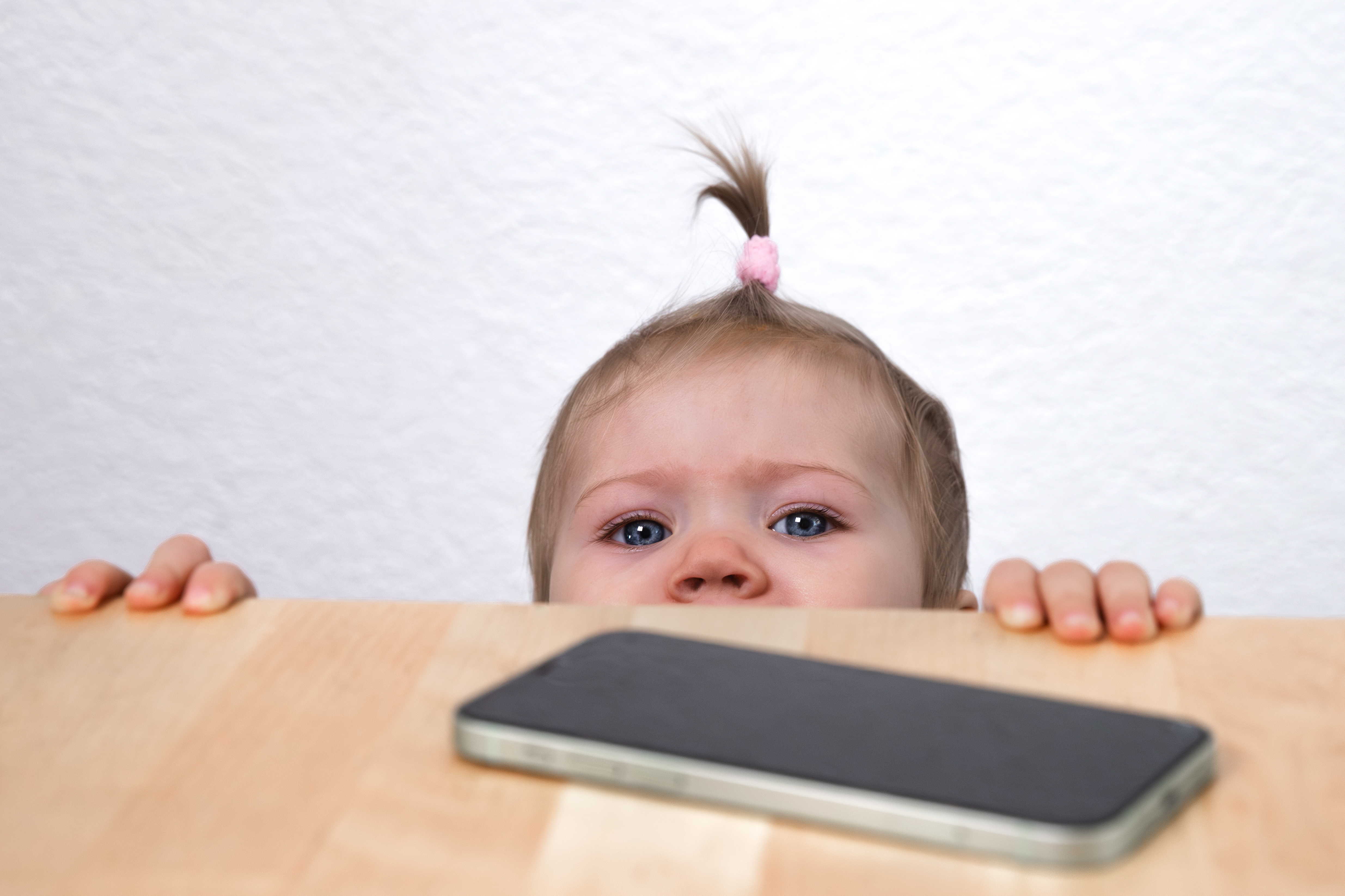 Baby looking up at a mobile phone on a table.