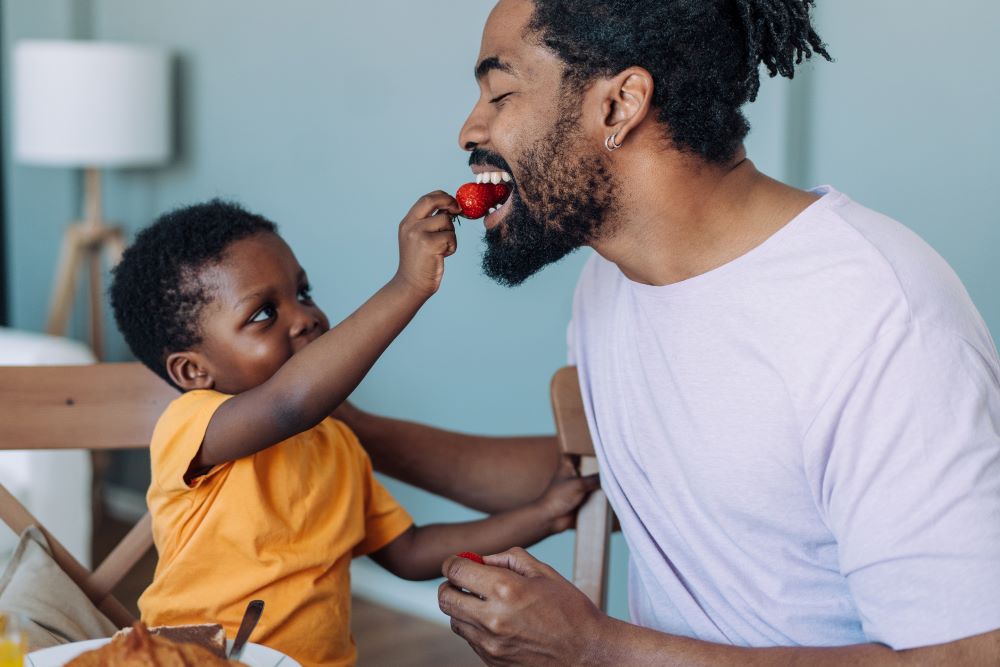Boy feeding his dad a strawberry.