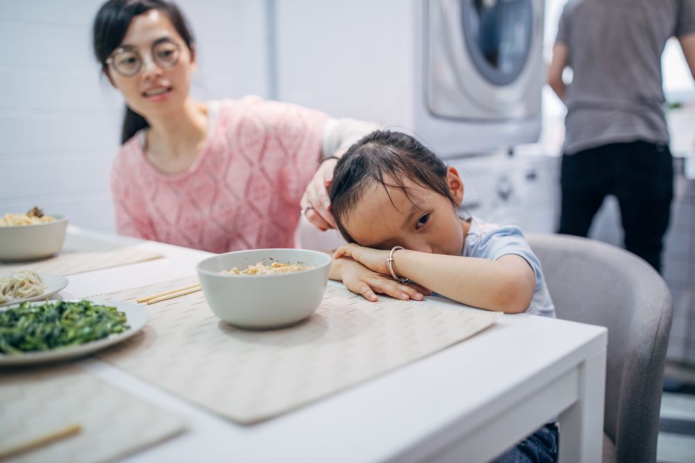 Child hiding their face at the dinner table.