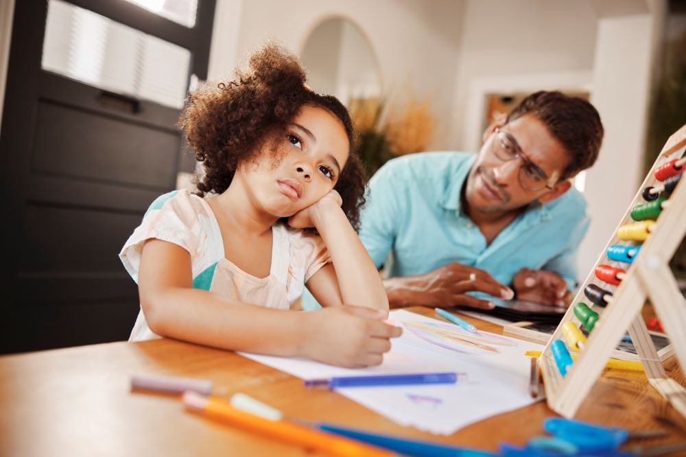 Father helping daughter with her homework, while she is staring into the distance.