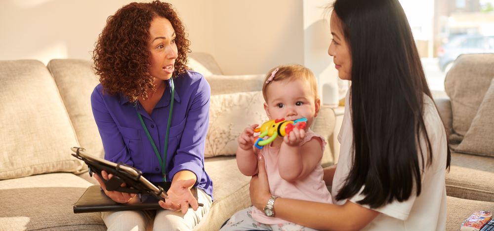 Health visitor chatting to mum with baby on her knee. 