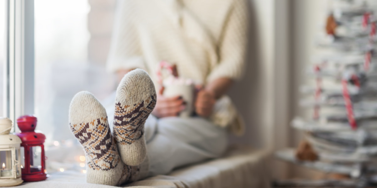 Woman sitting on a windowsill holding a mug of tea and wearing warm winter socks