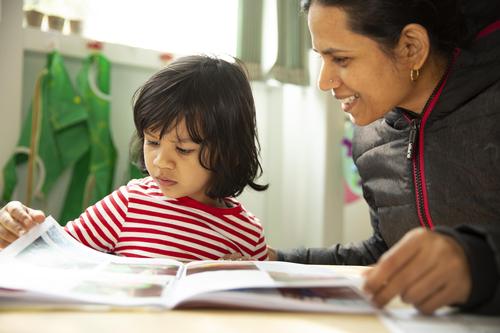Image of a child and a woman sitting together at a table in a playroom looking at a book.