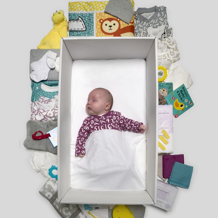 Baby asleep in the Baby Box, surrounded by items from the box