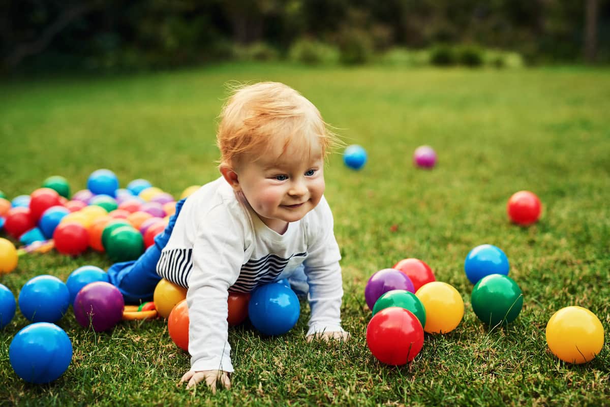 Photo of a baby crawling with balls on grass 