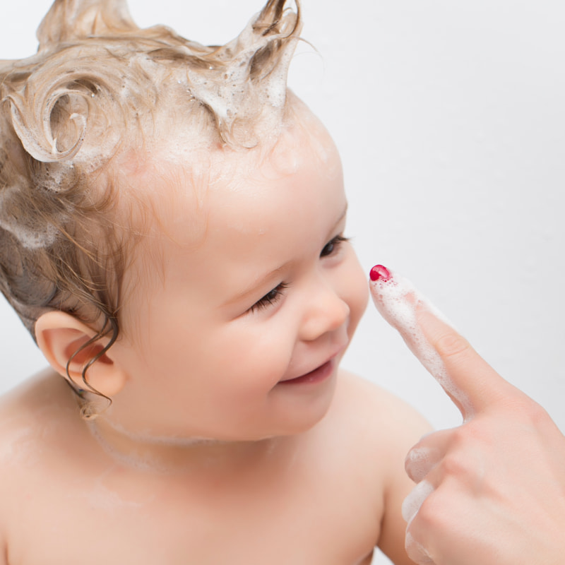 Image of a mum tapping a smiling baby's nose, the baby has bath bubbles in their hair.