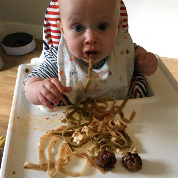 baby in highchair eating pasta noodles
