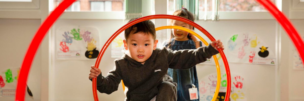 Image of a boy climbing through a red hula hoop, with a girl standing behind him.