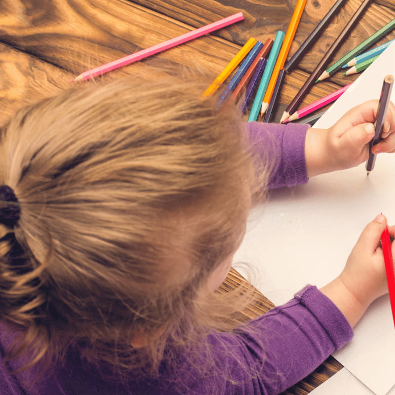 Image of a child drawing on paper with colouring pencils.