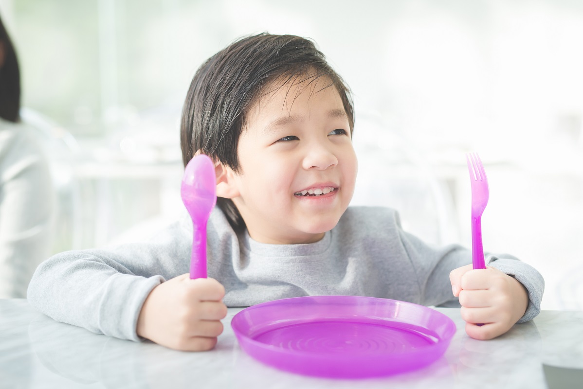 Child holding a plastic knife and fork