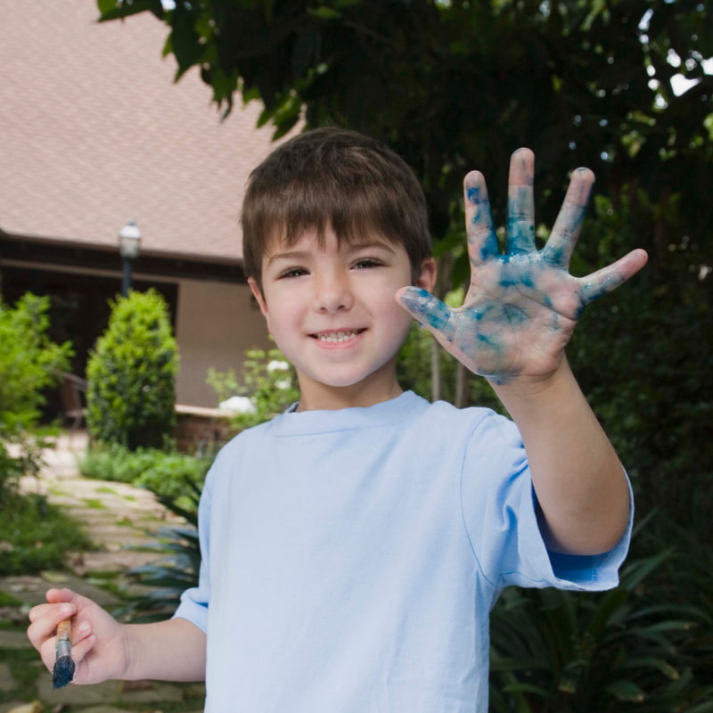 Image of a child smiling and waving at the camera with a hand covered in paint.