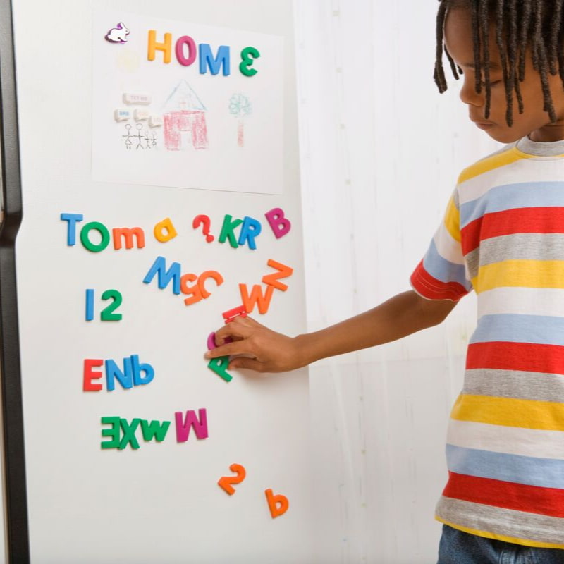 Image of a child spelling words on a white board using colourful letter magnets.