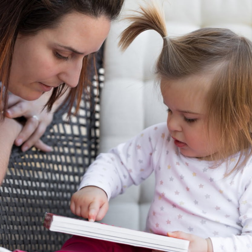 Image of a child pointing to a page of a book that she and her mum are both looking at.