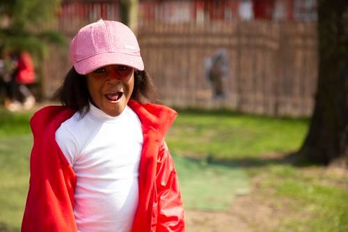 Image of a child outside, smiling at the camera and wearing a pink cap.