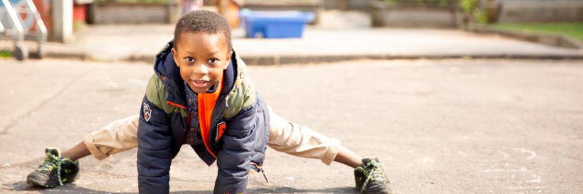 Image of a child doing the splits in a playground while looking at the camera.