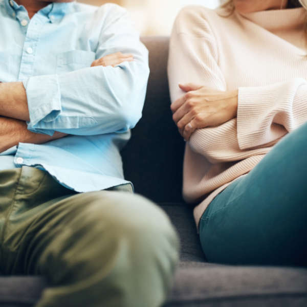 Photo of a couple sitting on a couch arms crossed not touching 