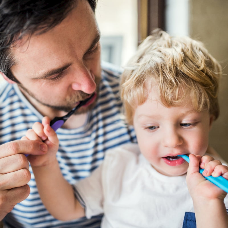Image of a dad and toddler brushing their teeth together.