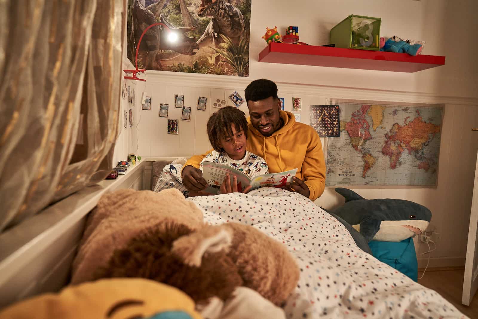 Image of a dad and child sitting next to each other in a bedroom, reading a book.