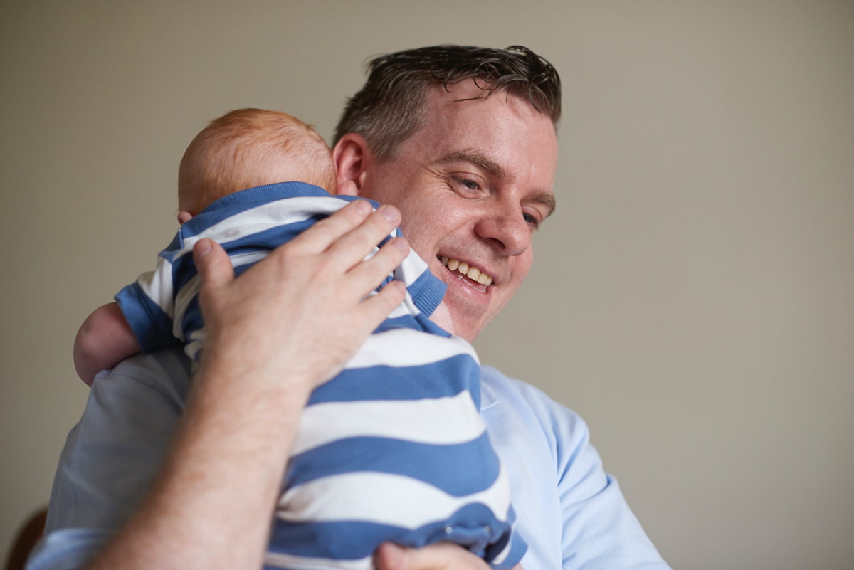 Image of a dad smiling while holding a baby.