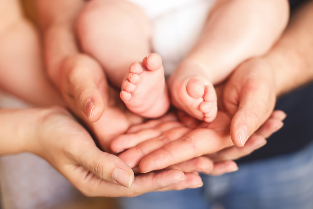Image of four adult hands and a baby's feet.