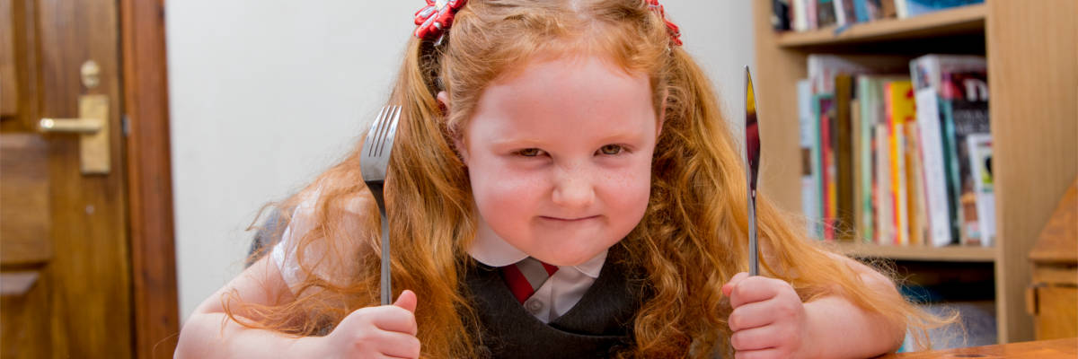 Girl with pigtails holding up her knife and fork