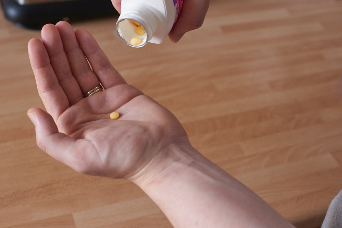 Image of the palm of a hand with one vitamin tablet on it.
