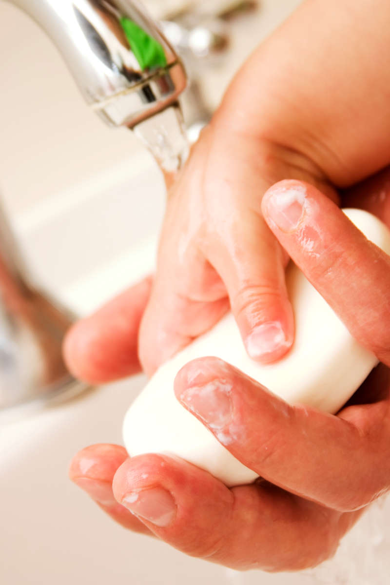 Image of a toddler and an adult's hands under a tap holding soap.